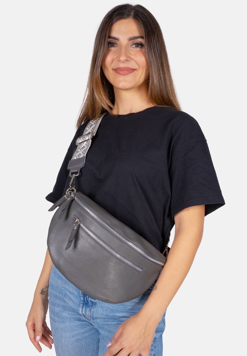 Sac banane en cuir gris avec une finition texturée, deux poches zippées et une sangle réglable à motifs, porté en bandoulière.