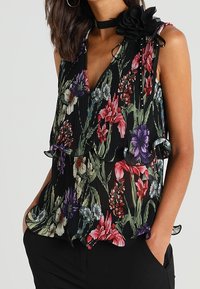 Blusa a fiori nera, con scollatura a V profonda, texture plissettata, bordi arricciati e un accento floreale nero sulla spalla.