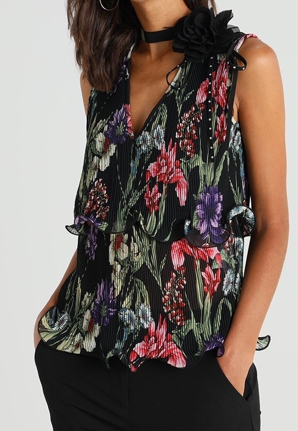 Blusa a fiori nera, con scollatura a V profonda, texture plissettata, bordi arricciati e un accento floreale nero sulla spalla.