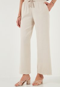 Helle beige weite Hosen mit elastischem Bund und Kordelzug. Hat einen strukturierten Stoff und fransige Saumakzente.