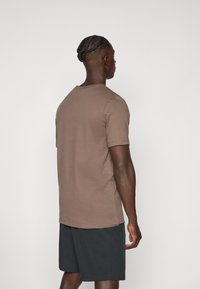 T-shirt en coton marron à manches courtes et col rond, associé à un short sombre. Texture lisse, design minimal, vue de dos simple.