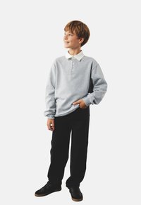 Sudadera gris con cuello blanco, tapeta de tres botones, mangas largas, combinada con pantalones negros y zapatillas negras, en pose de pie.