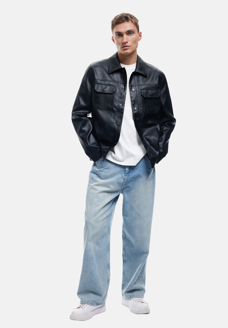Sort læderjakke med to forlommer, parret med lyseblå brede denimbukser og hvide sneakers. En ensfarvet hvid t-shirt under.
