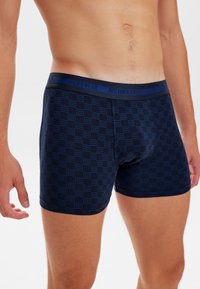 Modré boxerky s potiskem a měkkým elastickým pasem označené "JBS UNDERWEAR." Materiál vypadá prodyšně a těsně sedí.