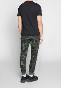 Svart t-shirt med kort ärm kombinerad med gröna kamouflerade byxor. Byxorna har midjeband av elastiskt material och smalnande manschetter. Svarta sneakers fulländar looken.