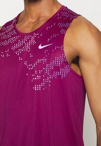 Nike träningslinne i mörkrosa med ett gradientmönster av små blå prickar. Har en rund halsringning och är ärmlös.