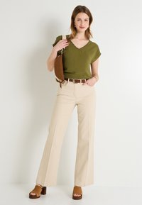 Haut court texturé vert olive à col en scallop, associé à un pantalon large beige et des sandales à talons brunes. Ceinture et sac bruns.