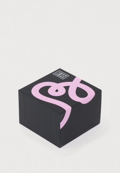 Čierna štvorcová krabica s ružovým kurzívnym dizajnom a malým bielym logom v hornom rohu. Matný povrch, minimalistický dizajn.