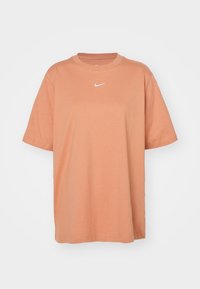 Pomarańczowa koszulka z krótkim rękawem z bawełny, z okrągłym dekoltem i małym, białym logo Nike na piersi. Prosty krój.