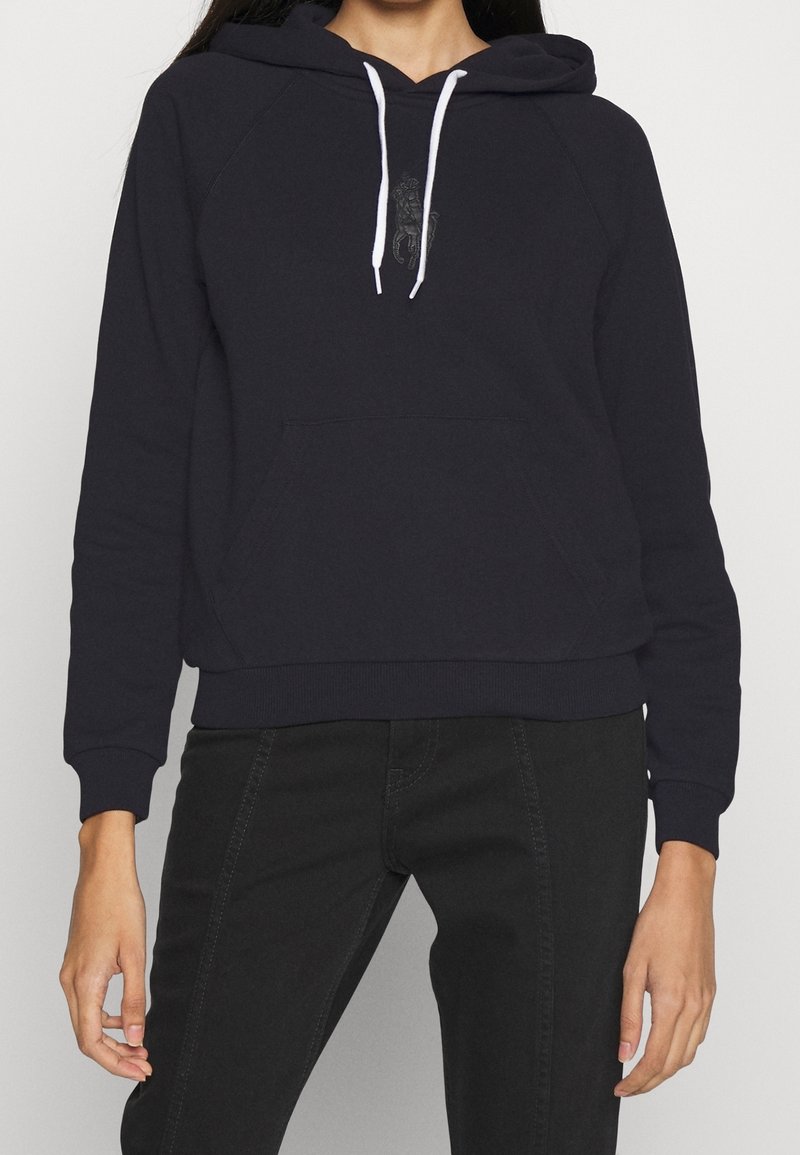 Marinblå hoodie med framficka, vita dragband och broderad design på bröstet. Har ribbade ärmslut och nederkant.