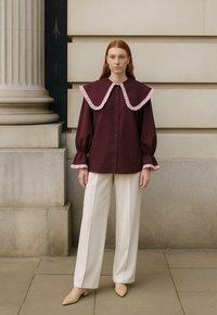 Bordeaux shirt met een grote roze gerimpelde kraag, knoopsluiting aan de voorkant en pofmouwen. Gecombineerd met crèmekleurige wijde broek en beige hakken.