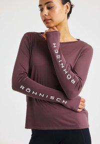 Langärmliges, lila Sportoberteil aus glattem, dehnbarem Stoff mit "RÖHNISCH" in Weiß entlang des Ärmels aufgedruckt.
