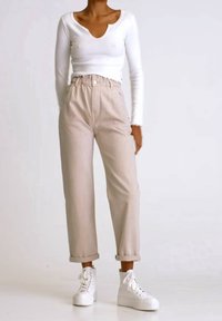 Blusa blanca de manga larga con escote redondeado, combinada con pantalones de tiro alto de pierna ancha en un tono beige claro y zapatillas de plataforma blancas.