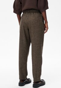 Bruine, gestructureerde broeken met een rechte snit, zijvakken en een tailleband met riemlussen. Gecombineerd met donkere schoenen.