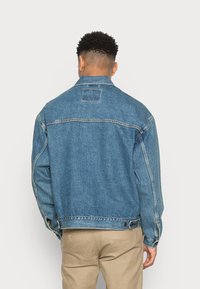 Jeansjacka i mellanblått, med klassisk krage, knappstängning, kontrasterande sömmar och sidofickor. Avslappnad passform med texturerad yta.