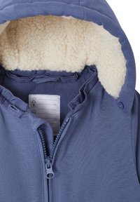 Blue outer shell jacket featuring a fuzzy cream-colored lining in the hood. Includes a zipper, buttons, and a care label inside.