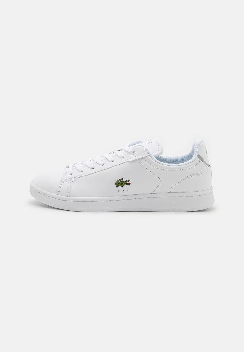 Sneaker in pelle bianca con una texture liscia, dotata di design con lacci, punta rotonda e logo Lacoste verde sul lato. Stile minimalista.