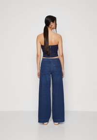 Haut sans manches en denim foncé avec fermeture éclair dans le dos, associé à un pantalon large en denim foncé avec poches latérales et arrière.