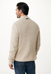 Beige ribbad tröja med hög krage, med en svart detalj vid nacken, kombinerad med blå jeans. Strukturerad tyg och avslappnad passform.