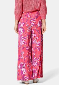 Pantalons larges fleuris en rose avec des motifs floraux violets et blancs. Fabriqués en tissu léger avec une taille élastique.