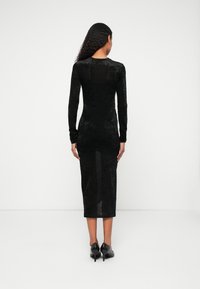 Rochie midi neagră cu mâneci lungi, dintr-un material texturat, cu o siluetă care se mulează pe corp, cu un decolteu adânc la spate și o ușoară transparență la marginea fustei.