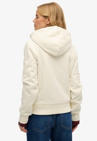 Felpa con cappuccio color crema con una texture morbida, polsini e orlo a coste, caratterizzata da una vestibilità rilassata e dettagli di cucitura sulle spalle.