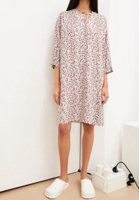 Robe florale avec une coupe ample, un décolleté en forme de trou de clé et des manches trois-quarts. Les couleurs incluent le blanc, le rouge et le bleu sur un fond clair.