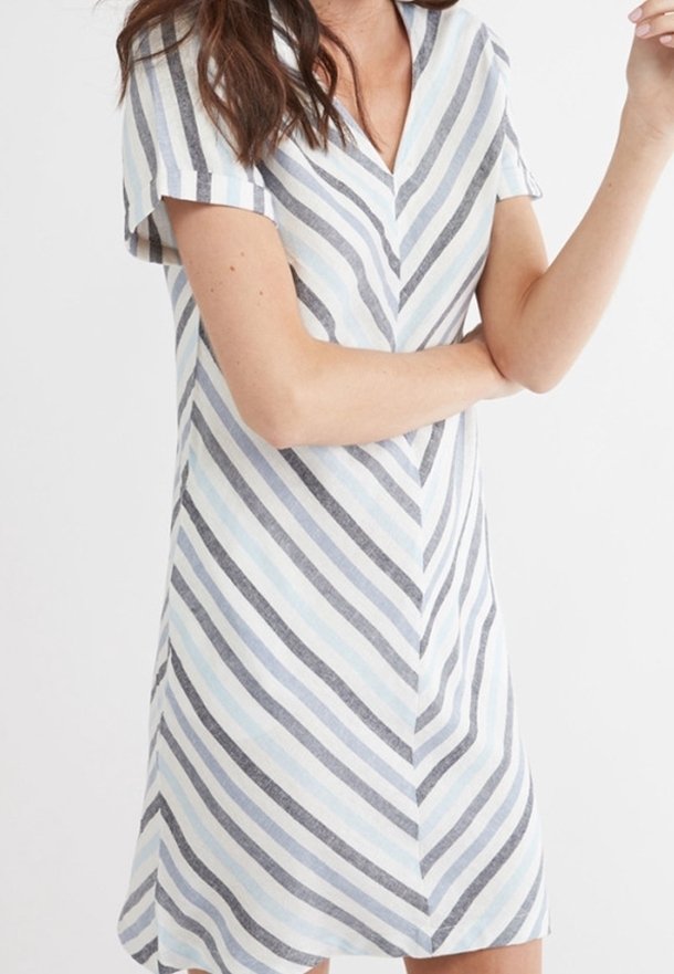 Femme portant une robe à manches courtes et col en V avec des rayures diagonales bleu clair, grises et blanches, debout devant un fond blanc uni.
