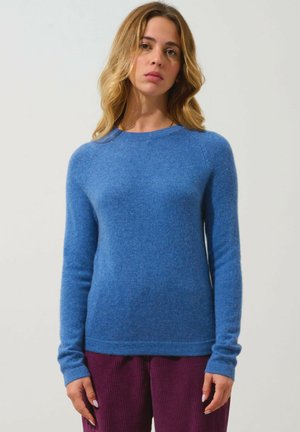 Maglione di lana blu con maniche lunghe e scollatura rotonda. Texture morbida e forma aderente, abbinato a pantaloni di corduroy viola a coste.