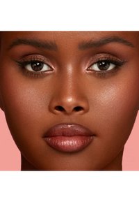 Gros plan d'un visage à la peau noire, présentant une texture lisse, des lèvres pleines d'une douce teinte marron, des sourcils bien dessinés et des pommettes mises en valeur.
