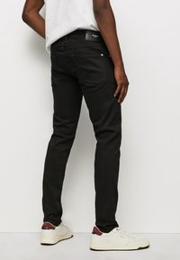 Jeans de mezclilla negra con un corte ajustado, que cuentan con un parche trasero de cuero, herrajes plateados y un diseño minimalista. Combinados con zapatillas blancas.