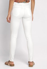 Witte skinny jeans van rekbare stof, met twee achterzakken en een gladde afwerking, gecombineerd met een gestreept topje en sandalen.