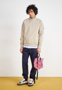 Beiger Sweater mit gerippten Bündchen, marineblaue Jogginghose und rosa Rucksack. Hat einen gestuften Look mit einem weißen gestreiften Shirt darunter.