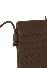 Brun läderclutch med vävd textur, som har en dragkedjestängning upptill och ett flexibelt band för enkel bärbarhet.