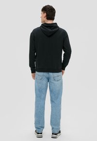 Sudadera negra con capucha y mangas largas, acompañada de jeans rectos de color azul claro. El conjunto se completa con zapatillas negras y blancas.