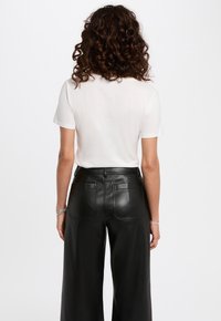 Witte, kortemouwen t-shirt gecombineerd met hooggaande, zwarte faux leren wijde broek met achterkantzakken en een gladde textuur.