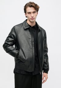 Giubbotto bomber in ecopelle nera con zip frontale, polsini a costine e tasche laterali, caratterizzato da una texture liscia e da una silhouette classica.