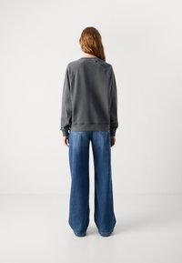 Felpa grigia con maniche raglan e collo rotondo, abbinata a jeans in denim blu a gamba ampia, entrambi in una vestibilità rilassata.