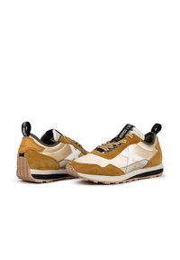 Sneakers featuring a tan suede and cream fabric upper, white accents, textured soles, and a pull tab at the heel for easy wear.