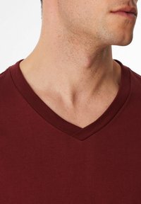 T-shirt bordeaux a scollo a V realizzato in morbido cotone. Presenta maniche corte e colletto a costine. Senza motivi o dettagli visibili.