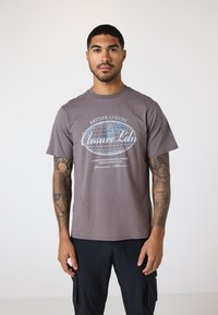Grå crew neck t-shirt lavet af bomuldsblanding. Forsiden har hvid dekorerende tekst og et globusgrafik. Korte ærmer, afslappet pasform.