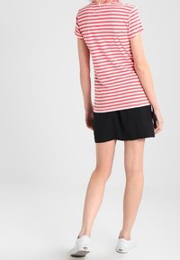 Camisa de manga corta a rayas rojas y blancas hecha de algodón suave, combinada con una falda negra. La persona lleva unas zapatillas blancas.