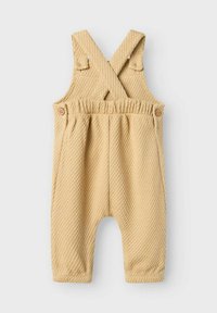 Romper in cotone giallo chiaro con un design testurizzato a nido d'ape. Spalline incrociate, bottoni in legno e vita elasticizzata; vestibilità ampia e gambe affusolate.