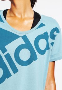 Lichtblauw katoenen T-shirt met een groot donkerblauw "adidas" logo. Het shirt heeft een ronde hals en korte mouwen.