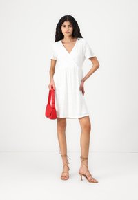 White A-line dress with short sleeves, V-neck, eyelet pattern, paired with a red handbag and gold strappy heels. Smooth fabric texture.