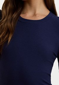 Námořnický žebrovaný top s kulatým výstřihem, který má texturovanou látku a těsný střih, s jemnými linkami a hladkým povrchem.