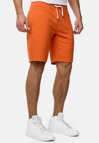 Orange bomuldsblandede shorts med elastisk talje, justerbart snor, sidelommer og en afslappet pasform, parret med hvide højtop sneaker.