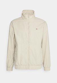 Béžová zipová bunda s stojáčkem, elastickými manžetami a lemem, na levé části hrudi s malým logem Tommy Hilfiger.