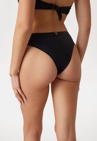 Black high-waisted bikini bottom with smooth texture, minimal seams, and a subtle logo accent on the rear.