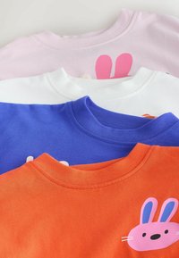 Štyri tričká s okrúhlym výstrihom naskladané na sebe: ružové, biele, modré a oranžové. Každé tričko má potlačený dizajn zajaca v rôznych farbách a štýloch.